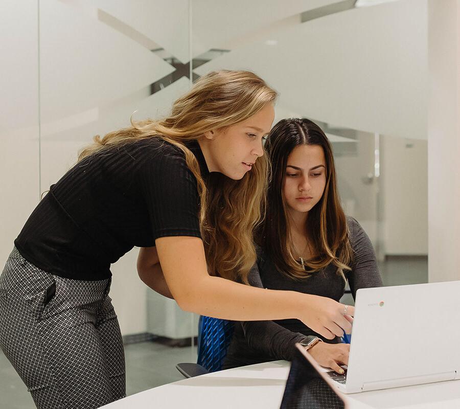 two students look at a computer screen in the library